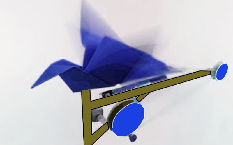 Ein aus blauem Papier gefalteter Origami-Vogel ist auf eine Unterkonstruktion mit Rädern geklebt. Außerdem ist eine Batterie an dem Objekt angeschlossen.