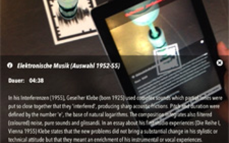 Ausstellungsansicht des Klangpfades. Ein Besucher liest auf einem Tablet Informationen zu Giselher Klebes Stück Interferenzen von 1955.