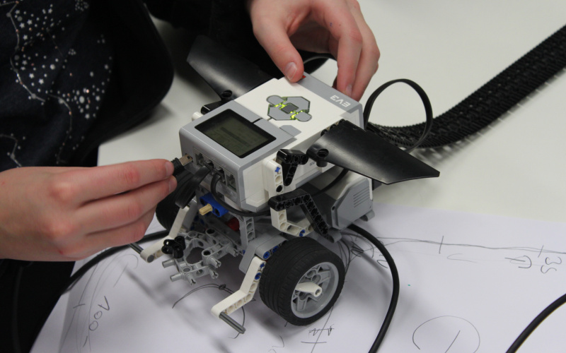 Ein Kind arbeitet an einem Lego-Roboter, gerade bringt es ein Kabel an der Vorderseite an.