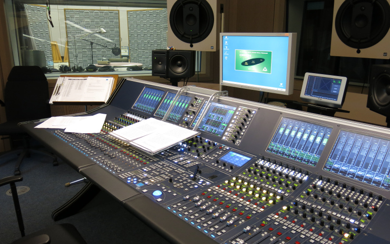 Das Foto zeigt ein Tonstudio mit Mischpult und Tonkabine im Hintergrund