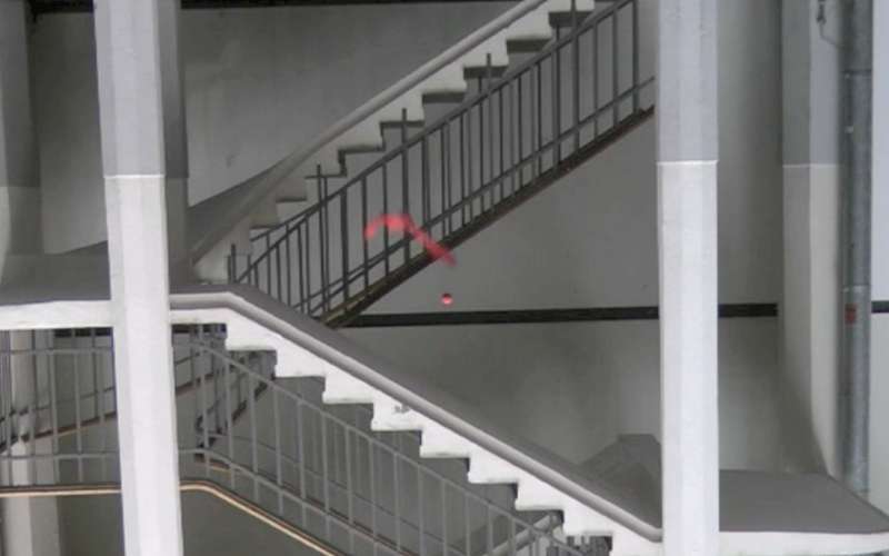 Ein Treppenhaus ist verkehrt herum zu sehen, ein roter Stoffstreifen und ein Ball scheinen nach oben zu fallen.