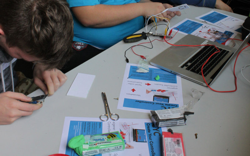 Ein paar Jungen sitzten gemeinsam am Tisch und arbeiten an einem Laptop und dem Bau eines Controllers.