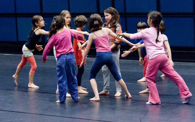 Eine Gruppe von Kindern bei einem Tanzworkshop stehen in einer lockeren Kreisformation.