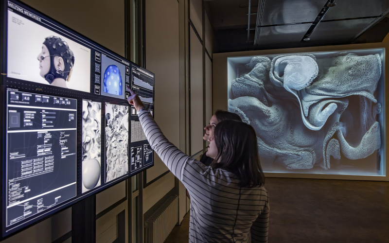 Two women stand in front of a screen in the exhibition »Open Codes. The World as a Field of Data«