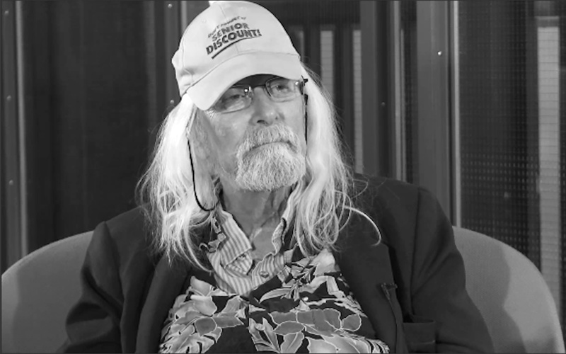 Portrait of Ira Schneider. He wears a baseball cap with the inscription "Senior Discount".