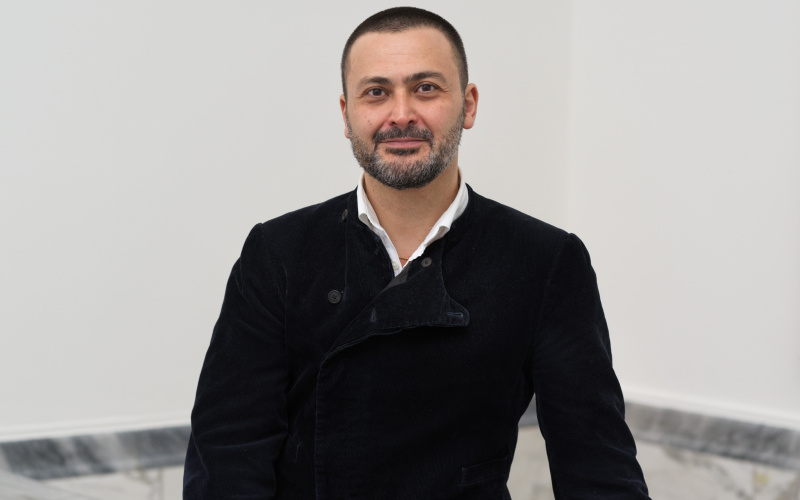 Portrait of Misal Adnan Yildiz sitting on a marble wall in front of a white wall