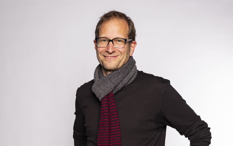 stehender lächelnder Mann mit Brille und grauem Schal