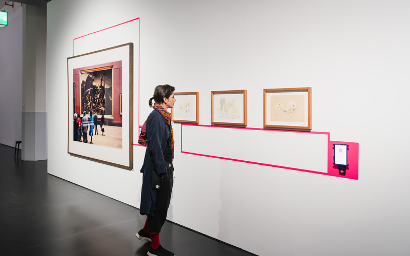 Eine Frau im Mantel betrachtet Bilder an einer weißen Wand.