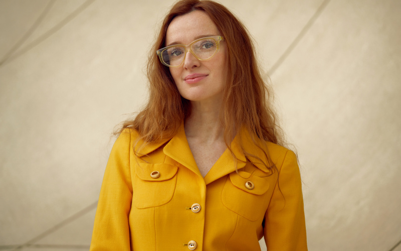 A woman with long red hair dressed in a yellow blouse.