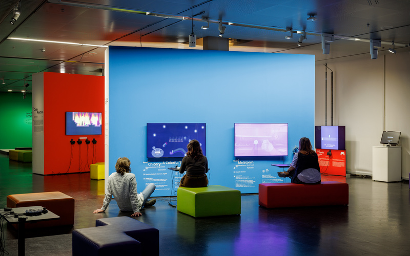 Three people can be seen in a room with several gaming stations.
