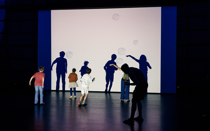 Vor einer Projektion schwebender Seifenblasen sind die Silhouetten mehrerer Kinder zu sehen.