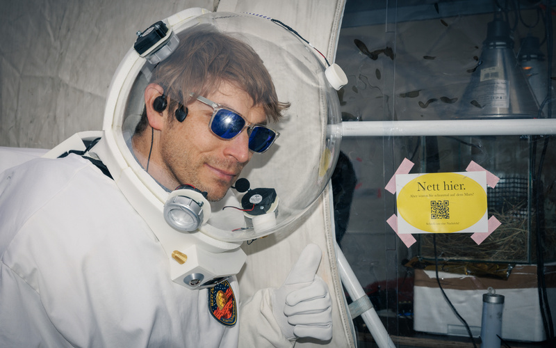 Das Bild zeigt eine Person, die eine Art Raumanzug und eine Sonnenbrille trägt.