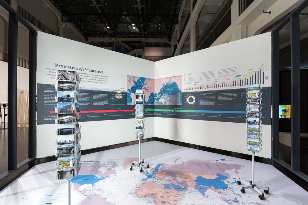 Postcards are in a stator and on the wall a graph with a world map and a lot of text can be seen