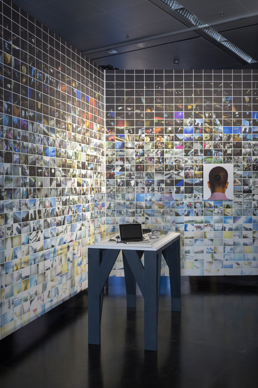 A rear wall with many small photos. In the foreground: A laptop on a table