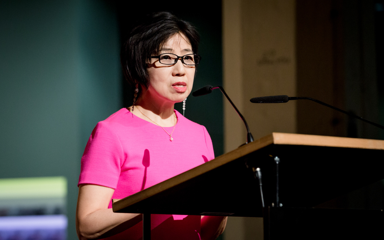 A woman dressed in a pink dress talks to the audience