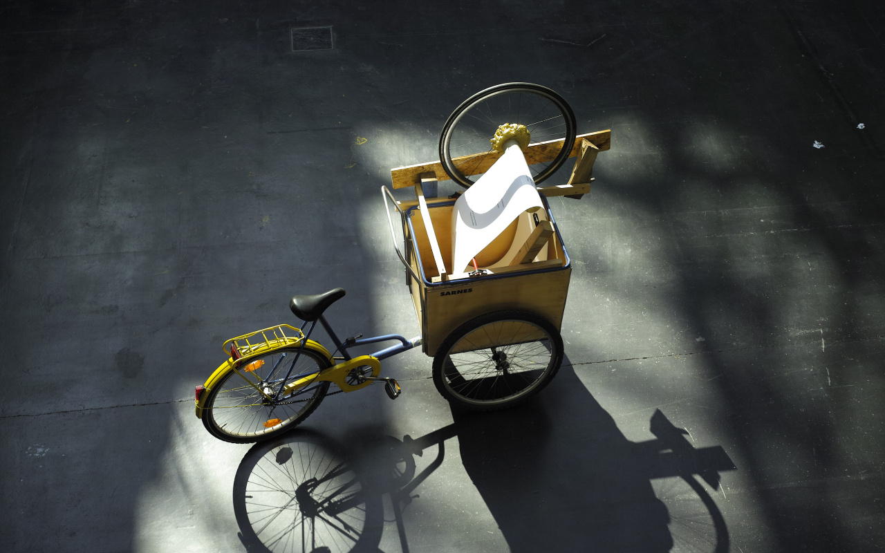 Das Lesefahrrad ist auf einem selbstgebauten Lastenfahrrad aufgebaut. Einige Holzreste sind hinzugefügt, einige Schrauben, ein Rad von einem kaputten Fahrrad, allgemeine Reste aus dem Lebensprozess, Gegenstände, die einst Teil von etwas Größerem waren.