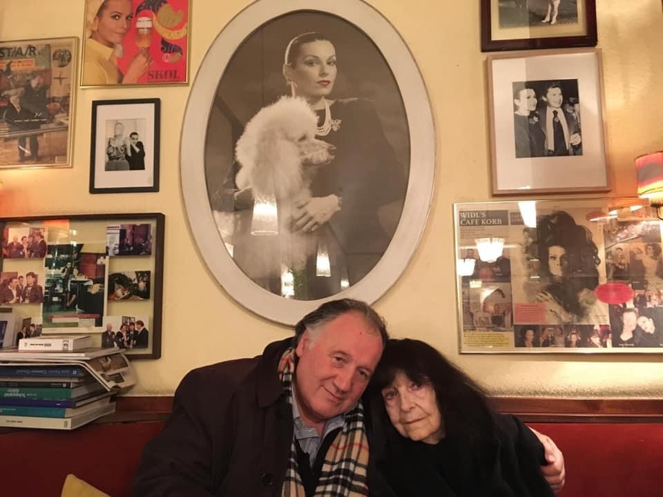 Peter Weibel with Friederike Mayröcker in front of a portrait by Susanne Widl at Café Korb, Vienna 2018.
