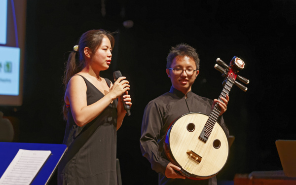 A woman with a microphone and a man with a kind of guitar