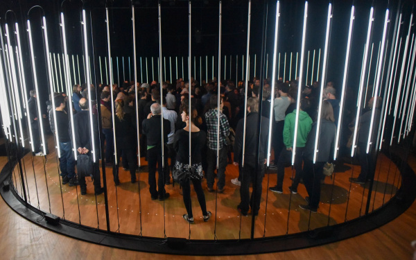 A circle of glowing neon tubes, many people standing in it