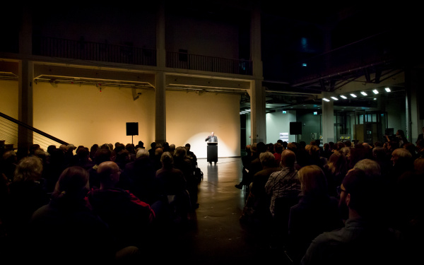 A man stands at a desk and talks to the audience