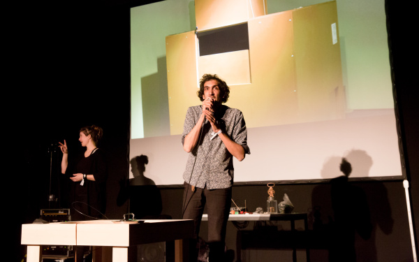 A man talks into a microphone. In the background: An interpreter for the deaf