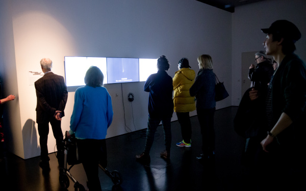 People stand in front of three monitors