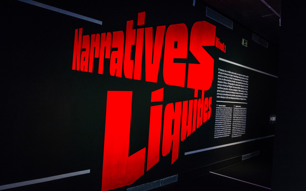 Der Schriftzug »Narratives Liquides« ist in großen roten Buchstaben in schräglage zu sehen. Rechts beginnt der Ausstellungseingang.