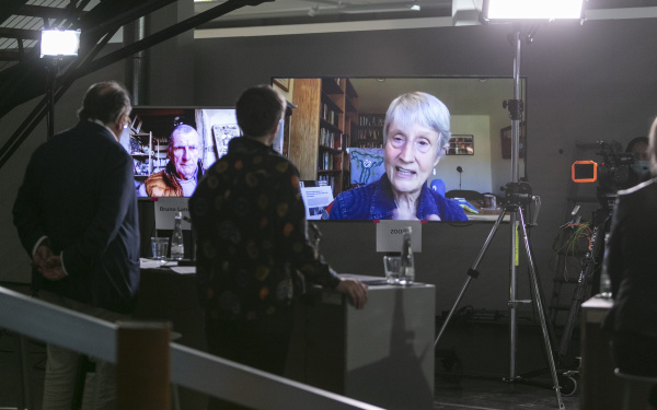 Donna Haraway ist auf einem großen Bildschirm zu sehen. Auf einem weiteren großen Bildschirm ist Bruno Latour zu sehen.