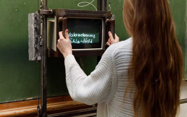 Besucherin vor Fietzeks »Tafel«, eine leere grüne Schultafel, auf der mit Hilfe eines Monitors zuvor unsichtbare Texte auftauchen.