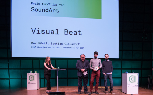 Three men and a moderator on stage