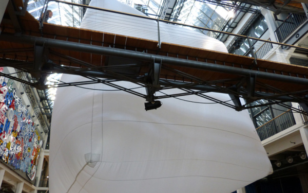 A very large white Baloon is hanging in an atrium