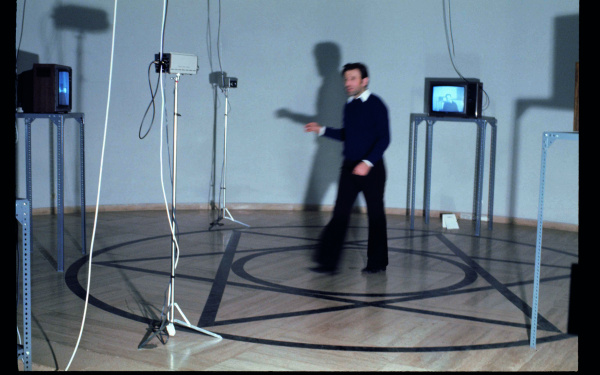 A man stands in a pentagram surrounded by monitors and cameras. The photo shows Peter Weibel as part of the exhibition »respektive Peter Weibel«.