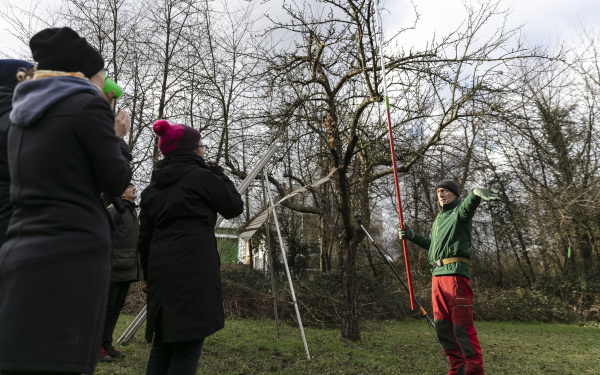 Ein Mann in Outdoor-Kleidung spricht vor eine Baum zu einer Gruppe.