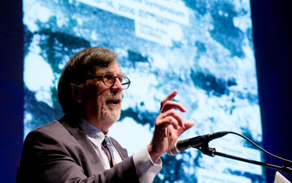Bruno Latour vor dem Globale Plakat. Er spricht ins Mikrofon.