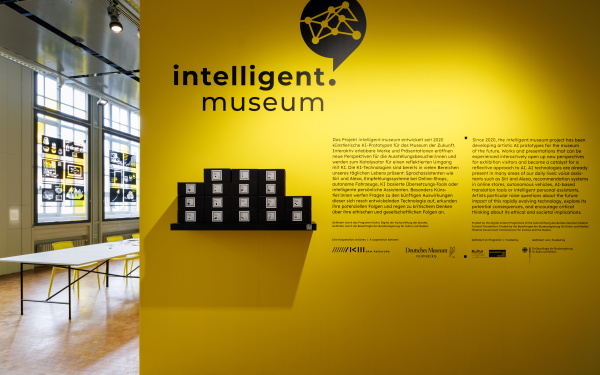 Zu sehen ist eine gelbe Wand mit dem Logo intelligent.museum und einem Einführungstext.