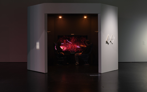 On display is the work "Haze Express". The picture shows two people looking at the work from one side each. It is the total view to see. The people are sitting in a small room where the work is and on a canvas you can see abstract shapes in red colors.