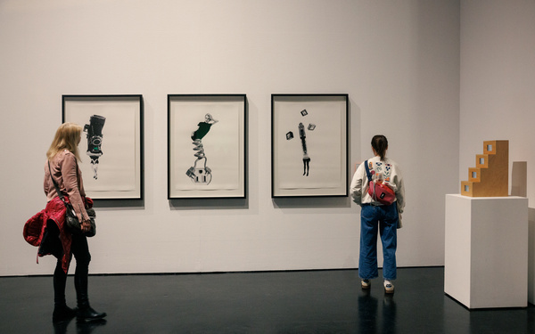 Several people look at a series of pictures on a wall in an exhibition room.