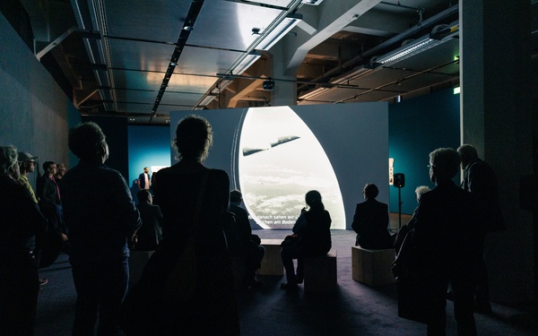Visitors can be seen in a darkened room watching a documentary film.