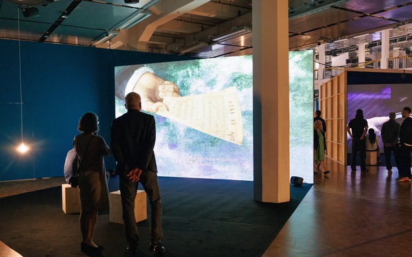  Two people can be seen standing in front of a large-format video projection.