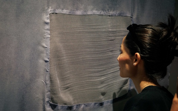 The picture shows a person looking at a work of art made of a net-like fabric.