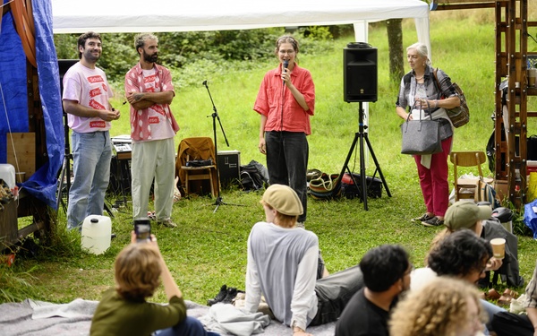 Zu sehen sind Menschen, die gemeinsam auf einer Wiese stehen und sitzen. 