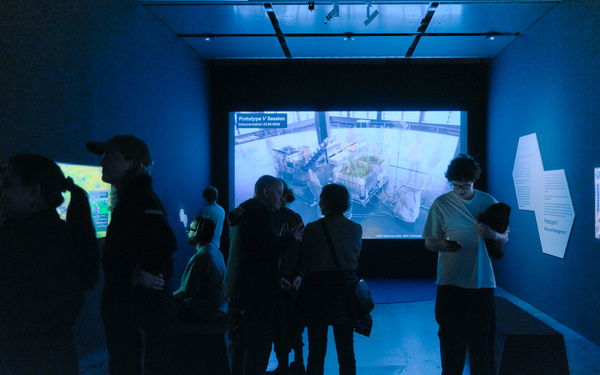Zu sehen ist ein dunkler Ausstellungsraum mit Projektionen an den Wänden. 