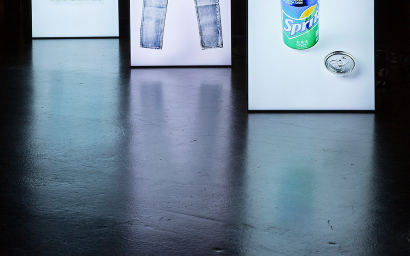Drei hintereinander stehende Leuchtständer, auf denen eine Hose, eine Sprite-Dose und ein Ausweis zu sehen sind