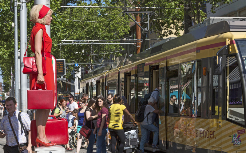 Eine Frau in Rot steht auf einem Stromkasten mitten in der Fußgängerzone