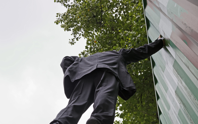 Ein Mann hängt in der Luft, hebt sich an einem Baucontainer mit nur einer Hand fest
