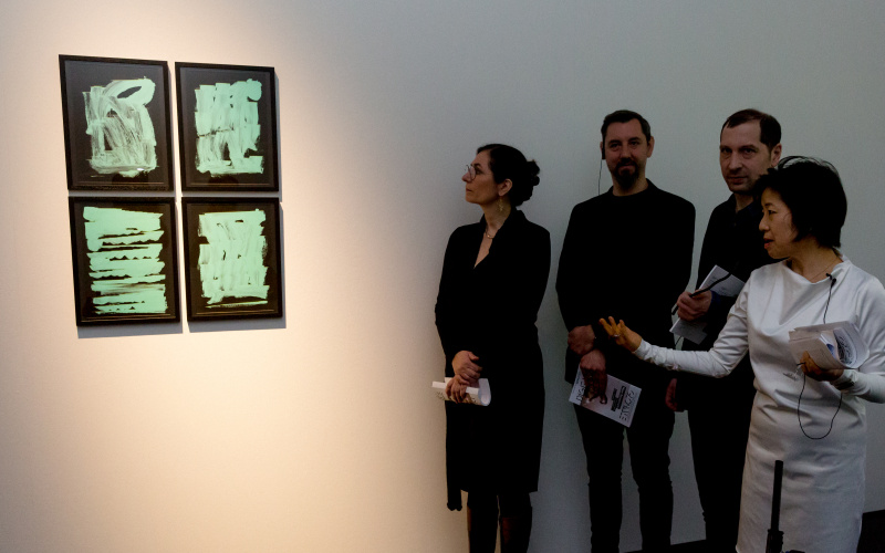 Vier Menschen betrachten vier Bilder, auf denen grüne Pinselstriche auf schwarzem Grund zu sehen sind