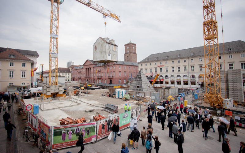 Ein Haus hängt an einem Kran inmitten einer großen Baustelle