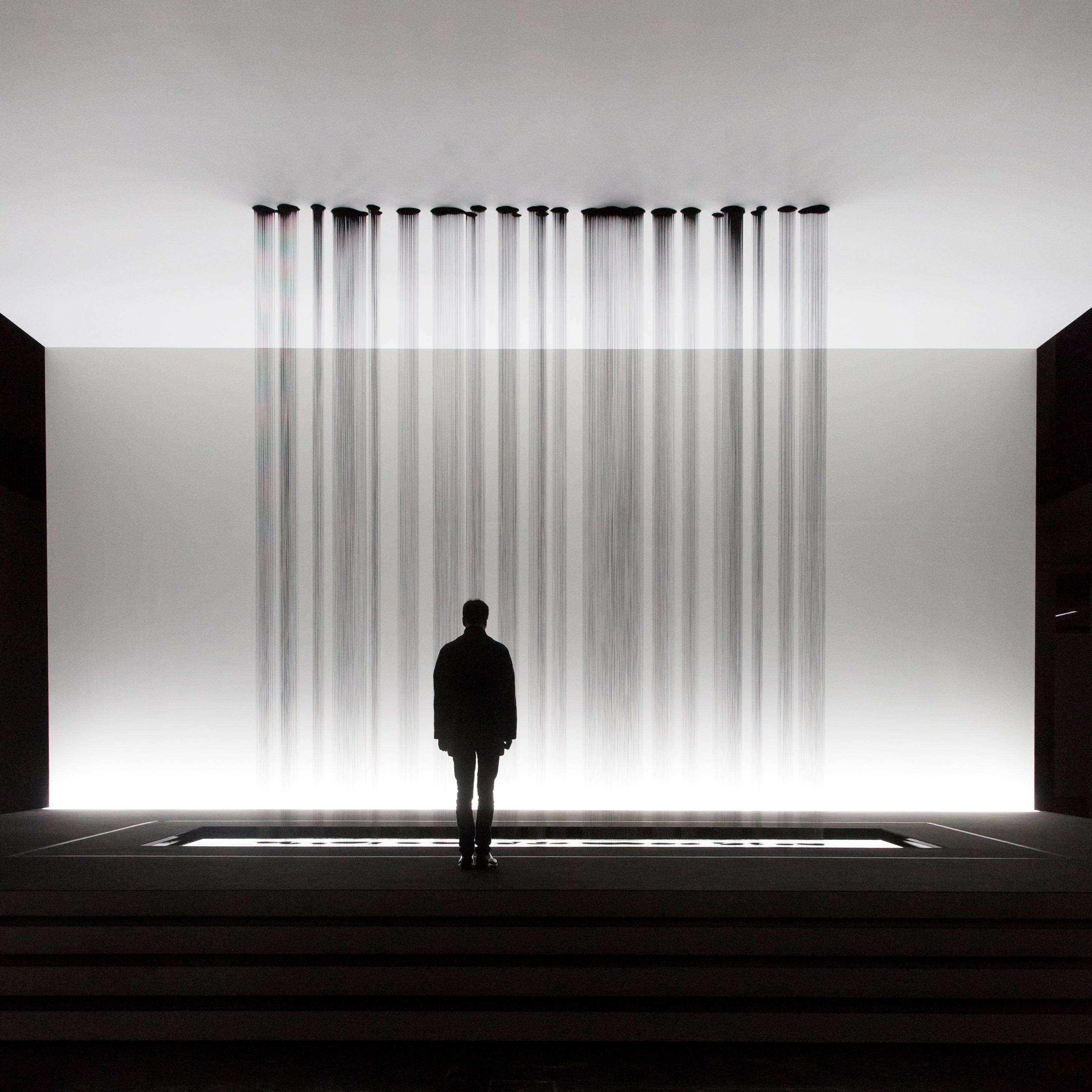 Eine Person steht vor einer Skulptur, bei der mehrere Rinnsale von Öl auf den Boden tropfen