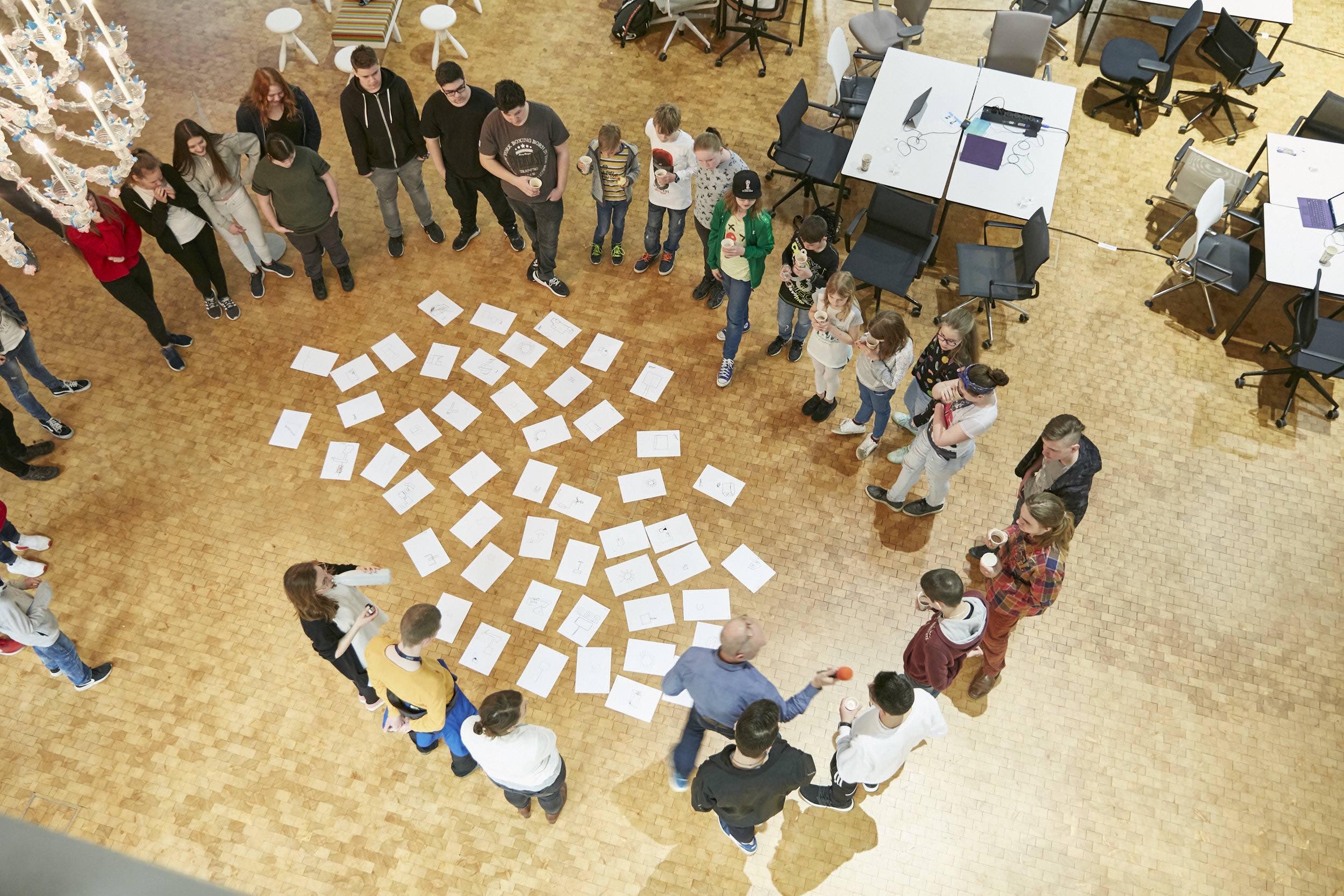 A group of young people stand around a collection of drawings in the exhibition room.