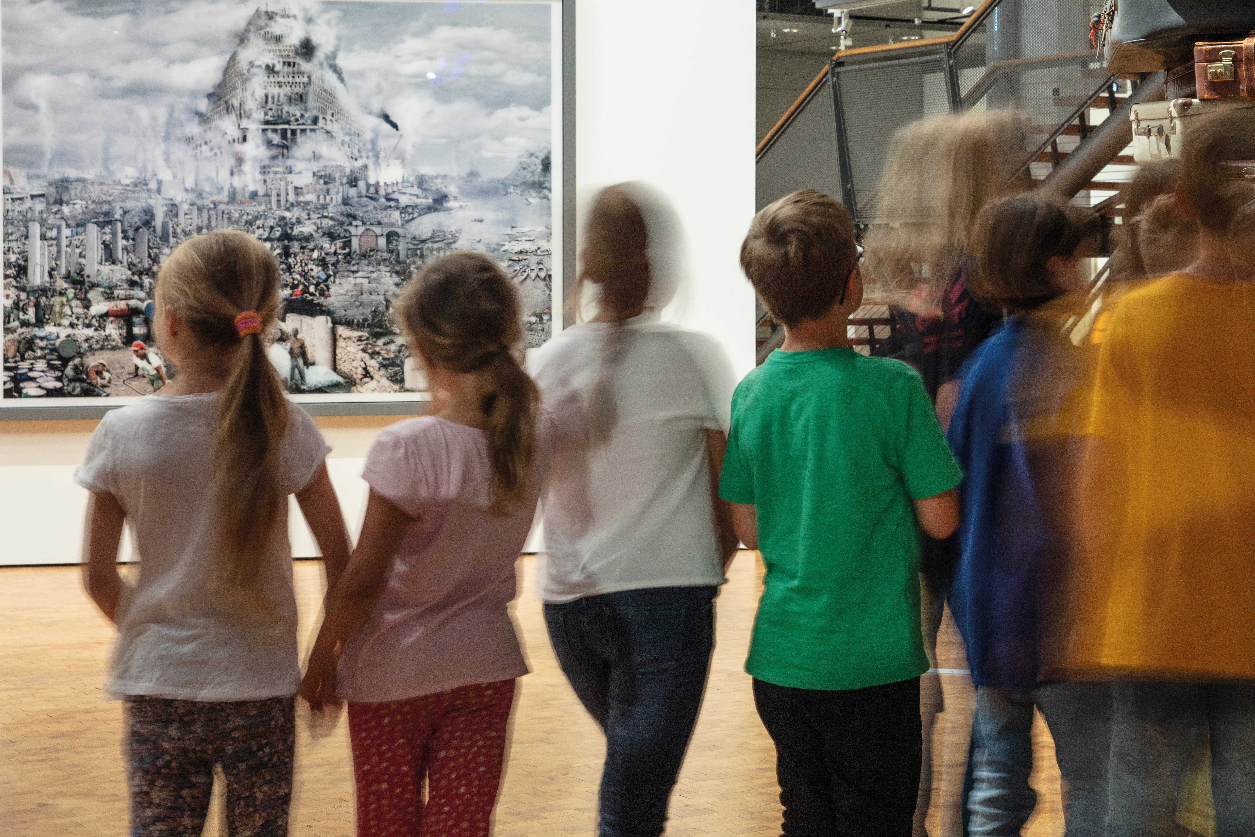Zu sehen sind eine verschommene Gruppe Kinder vor einem Bild, welches den Turm zu Babel zeigt.